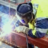 Svářeč v reflexní vestě svařuje ocelovou konstrukci ve výšce